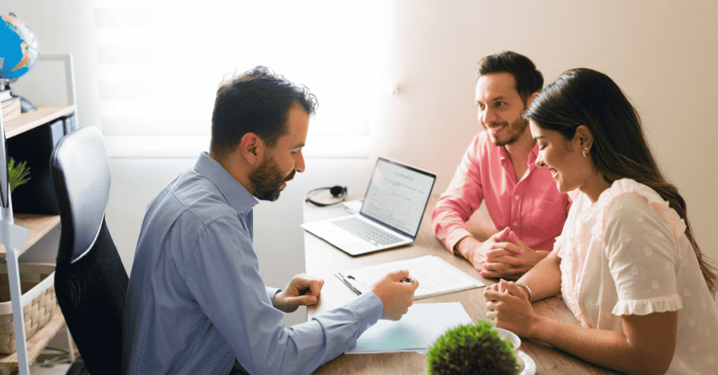 Casal sentado diante de um consultor, revisando documentos e recebendo orientações para contratar um empréstimo.