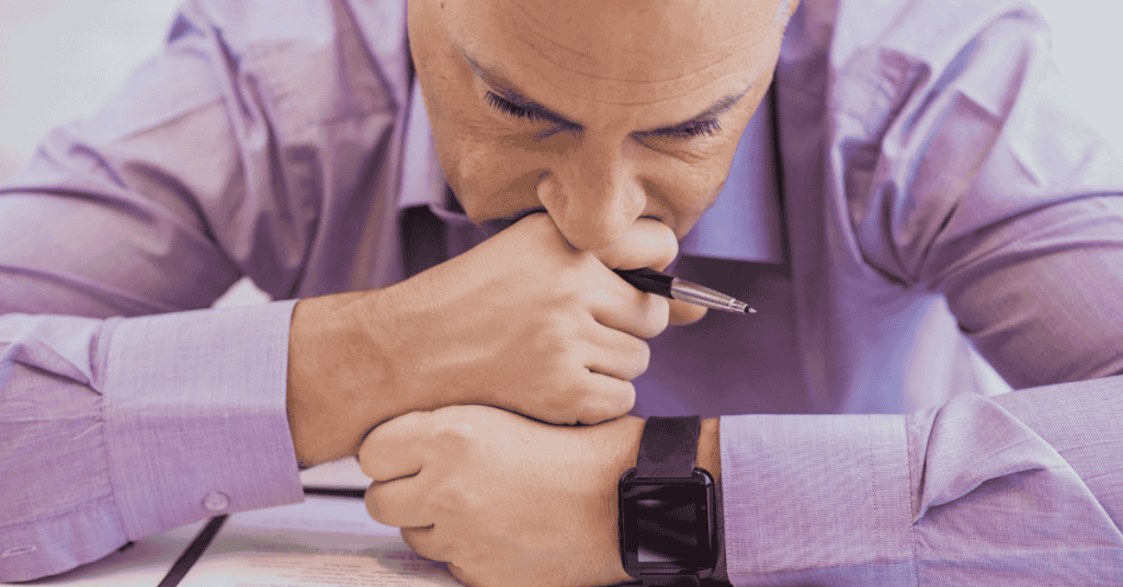 Homem com expressão preocupada apoiando a cabeça nas mãos enquanto analisa documentos relacionados a um empréstimo.